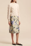 Woman wearing a cream Alpaca Chainette Sweater with cable knit design paired with a floral print midi skirt and black flats against a beige background.